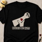 Black t-shirt printed BRUISED BUT HAPPY in ransom-note lettering below a raised fist with a red guitar pick on the forearm
