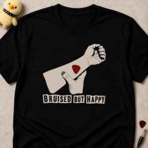 Black t-shirt printed BRUISED BUT HAPPY in ransom-note lettering below a raised fist with a red guitar pick on the forearm