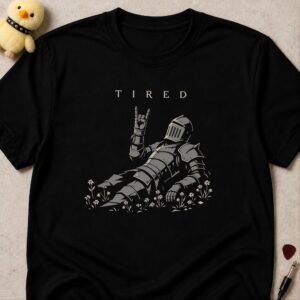 Black t-shirt printed TIRED above an armoured knight lying flat on his back in flowers throwing devil horns
