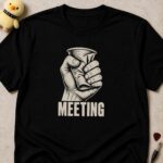 Black t-shirt printed MEETING below a clenched fist crushing a paper coffee cup