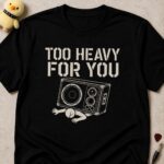 Black t-shirt printed TOO HEAVY FOR YOU above a person pinned flat under a fallen speaker cabinet