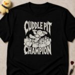 Black t-shirt printed CUDDLE PIT CHAMPION around a bandaged plush bunny on top of a pile of soft toys