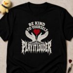 Black t-shirt printed BE KIND TO YOURSELF above two hands holding a red heart, and PLAY IT LOUDER in metal lettering below