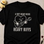 Black t-shirt printed A SOFT HEART NEEDS HEAVY RIFFS around a smiling cartoon heart playing an electric guitar