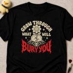 Black t-shirt printed GROW THROUGH WHAT WILL BURY YOU around a smiling flower growing from a gravestone, BURY YOU in dripping red letters