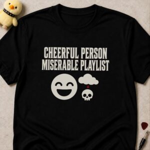Black t-shirt printed CHEERFUL PERSON MISERABLE PLAYLIST above a grinning smiley face beside a rain cloud dripping onto a small skull