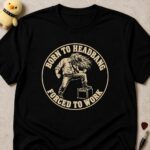 Black t-shirt printed BORN TO HEADBANG FORCED TO WORK in a cream circle around a headbanging office worker with one foot on an amp